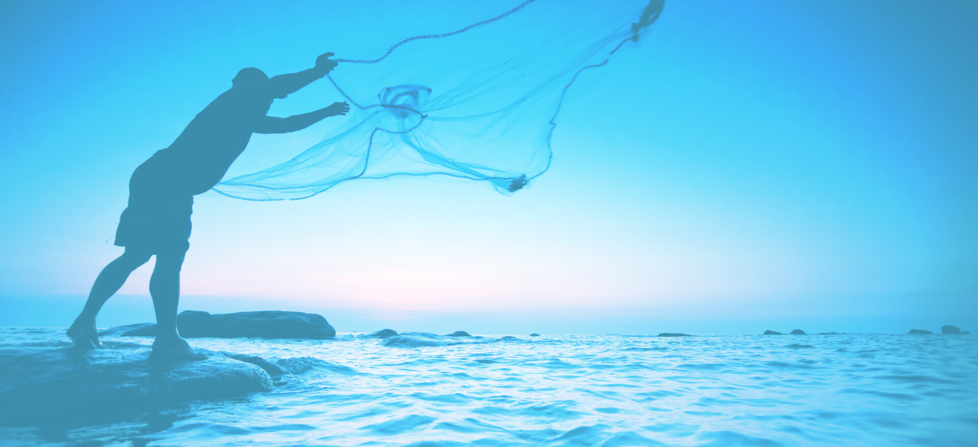 person standing on a rock casting a fishing net over rippled ocean